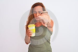 Middle age mature woman drinking a take away cup of coffee over isolated background pointing with finger to the camera and to you,