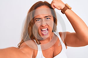 Middle age mature woman taking a selfie photo using smartphone over isolated background annoyed and frustrated shouting with
