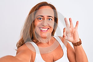 Middle age mature woman taking a selfie photo using smartphone over isolated background doing ok sign with fingers, excellent