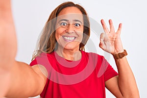 Middle age mature woman taking a selfie photo using smartphone over isolated background doing ok sign with fingers, excellent