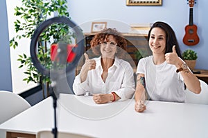 Middle age mother and daughter recording vlog tutorial with smartphone at home smiling happy and positive, thumb up doing