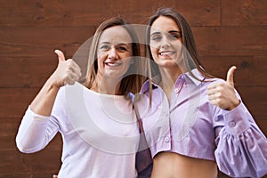 Middle age mother and young daughter standing over wooden background smiling happy and positive, thumb up doing excellent and