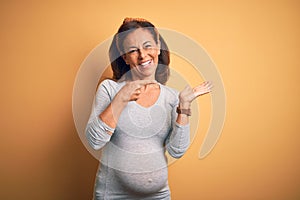 Middle age pregnant woman expecting baby at aged pregnancy amazed and smiling to the camera while presenting with hand and