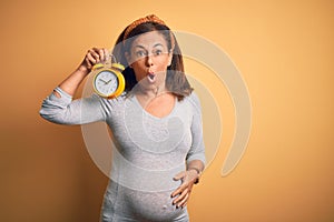 Middle age pregnant woman expecting baby at aged pregnancy holding alarm clock scared in shock with a surprise face, afraid and