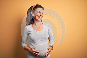 Middle age pregnant woman expecting baby at aged pregnancy looking away to side with smile on face, natural expression