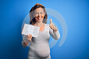 Middle age pregnant woman expecting baby boy over blue background happy with big smile doing ok sign, thumb up with fingers,