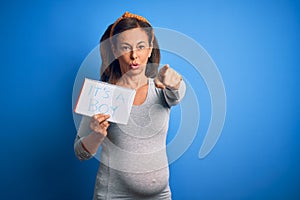 Middle age pregnant woman expecting baby boy over blue background pointing with finger to the camera and to you, hand sign,