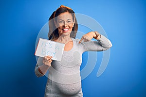 Middle age pregnant woman expecting baby boy over blue background with surprise face pointing finger to himself