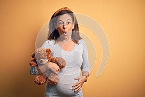 Middle age pregnant woman expecting baby holding teddy bear stuffed animal with a confident expression on smart face thinking
