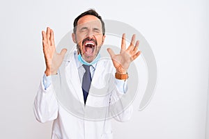 Middle age scientist man wearing coat and medical mask over isolated white background celebrating mad and crazy for success with