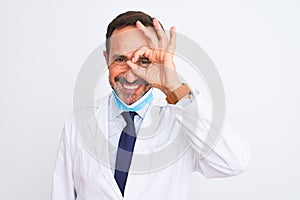 Middle age scientist man wearing coat and medical mask over isolated white background doing ok gesture with hand smiling, eye
