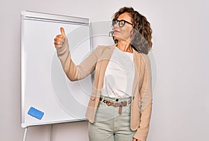 Middle age senior business woman standing on seminar presentation by magnectic blackboard Looking proud, smiling doing thumbs up