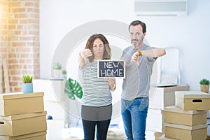 Middle age senior couple holding blackboard moving to a new home with angry face, negative sign showing dislike with thumbs down,