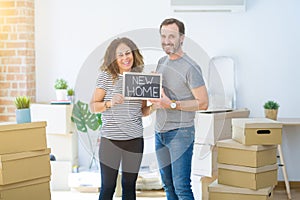 Middle age senior couple holding blackboard moving to a new home with a happy face standing and smiling with a confident smile