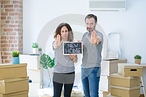 Middle age senior couple holding blackboard moving to a new home with open hand doing stop sign with serious and confident