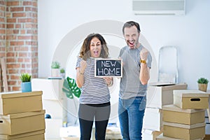 Middle age senior couple holding blackboard moving to a new home screaming proud and celebrating victory and success very excited,