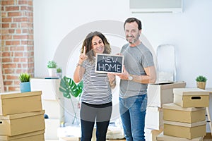 Middle age senior couple holding blackboard moving to a new home surprised with an idea or question pointing finger with happy