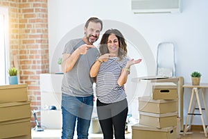 Middle age senior couple moving to a new home with boxes around amazed and smiling to the camera while presenting with hand and