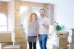 Middle age senior couple moving to a new home with boxes around amazed and smiling to the camera while presenting with hand and