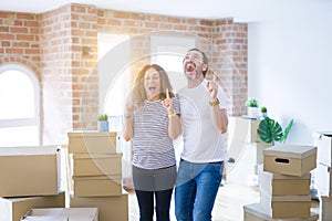 Middle age senior couple moving to a new home with boxes around amazed and surprised looking up and pointing with fingers and