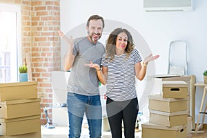 Middle age senior couple moving to a new home with boxes around clueless and confused expression with arms and hands raised