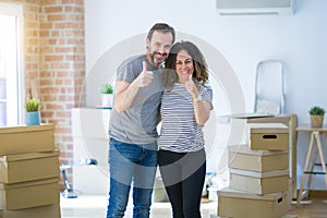 Middle age senior couple moving to a new home with boxes around doing happy thumbs up gesture with hand
