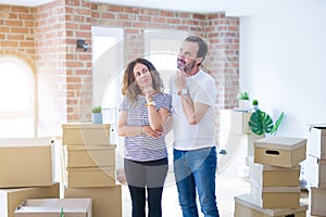 Middle age senior couple moving to a new home with boxes around with hand on chin thinking about question, pensive expression