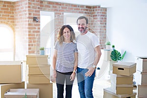 Middle age senior couple moving to a new home with boxes around with a happy and cool smile on face