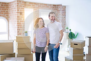 Middle age senior couple moving to a new home with boxes around looking away to side with smile on face, natural expression