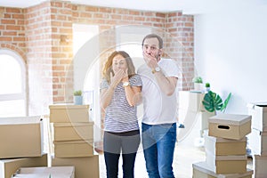 Middle age senior couple moving to a new home with boxes around shocked covering mouth with hands for mistake