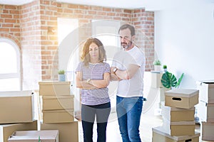 Middle age senior couple moving to a new home with boxes around skeptic and nervous, disapproving expression on face with crossed