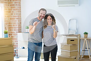 Middle age senior couple moving to a new home with boxes around smiling with happy face looking and pointing to the side with