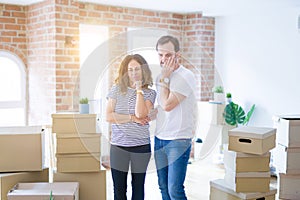 Middle age senior couple moving to a new home with boxes around thinking looking tired and bored with depression problems with