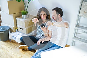 Middle age senior couple moving to a new home using smartphone with angry face, negative sign showing dislike with thumbs down,