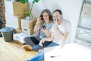 Middle age senior couple moving to a new home using smartphone doing ok sign with fingers, excellent symbol