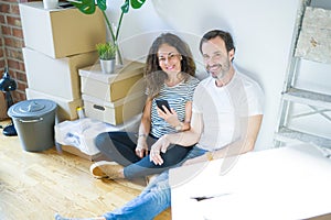 Middle age senior couple moving to a new home using smartphone with a happy face standing and smiling with a confident smile