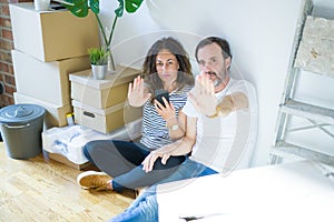 Middle age senior couple moving to a new home using smartphone with open hand doing stop sign with serious and confident