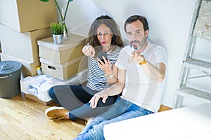 Middle age senior couple moving to a new home using smartphone pointing with finger to the camera and to you, hand sign, positive