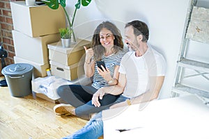 Middle age senior couple moving to a new home using smartphone pointing and showing with thumb up to the side with happy face