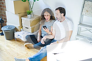 Middle age senior couple moving to a new home using smartphone scared in shock with a surprise face, afraid and excited with fear