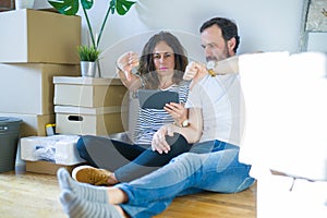 Middle age senior couple moving to a new home using tablet with angry face, negative sign showing dislike with thumbs down,