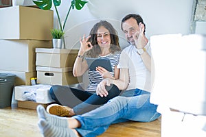 Middle age senior couple moving to a new home using tablet doing ok sign with fingers, excellent symbol