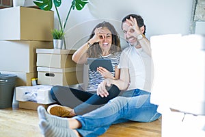 Middle age senior couple moving to a new home using tablet with happy face smiling doing ok sign with hand on eye looking through