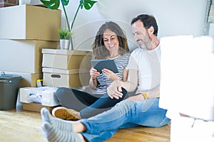 Middle age senior couple moving to a new home using tablet with a happy face standing and smiling with a confident smile showing