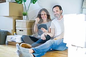 Middle age senior couple moving to a new home using tablet pointing and showing with thumb up to the side with happy face smiling