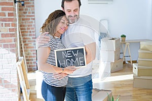 Middle age senior couple moving to a new house, smiling happy in love with apartmant holding a blackboard with new home text