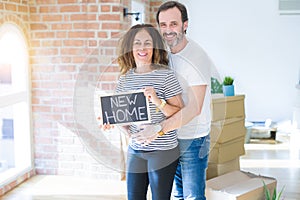 Middle age senior couple moving to a new house, smiling happy in love with apartmant holding a blackboard with new home text