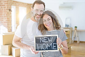 Middle age senior couple moving to a new house, smiling happy in love with apartmant holding a blackboard with new home text