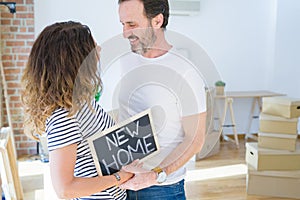 Middle age senior couple moving to a new house, smiling happy in love with apartmant holding a blackboard with new home text