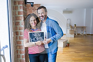 Middle age senior couple moving to a new house, smiling happy in love with apartmant holding a blackboard with new home text